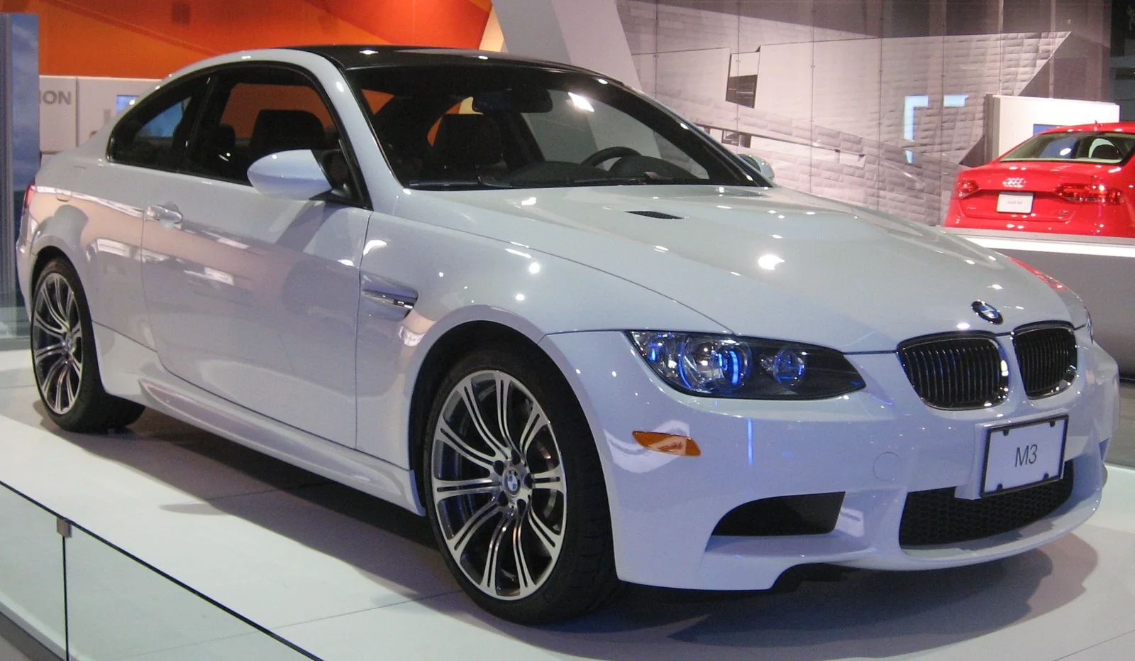 White BMW M3 E92 coupe displayed indoors, front three-quarter view.