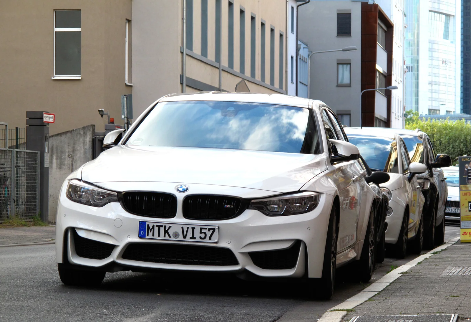 White BMW M3 F80 sedan parked on a city street, front three-quarter view.