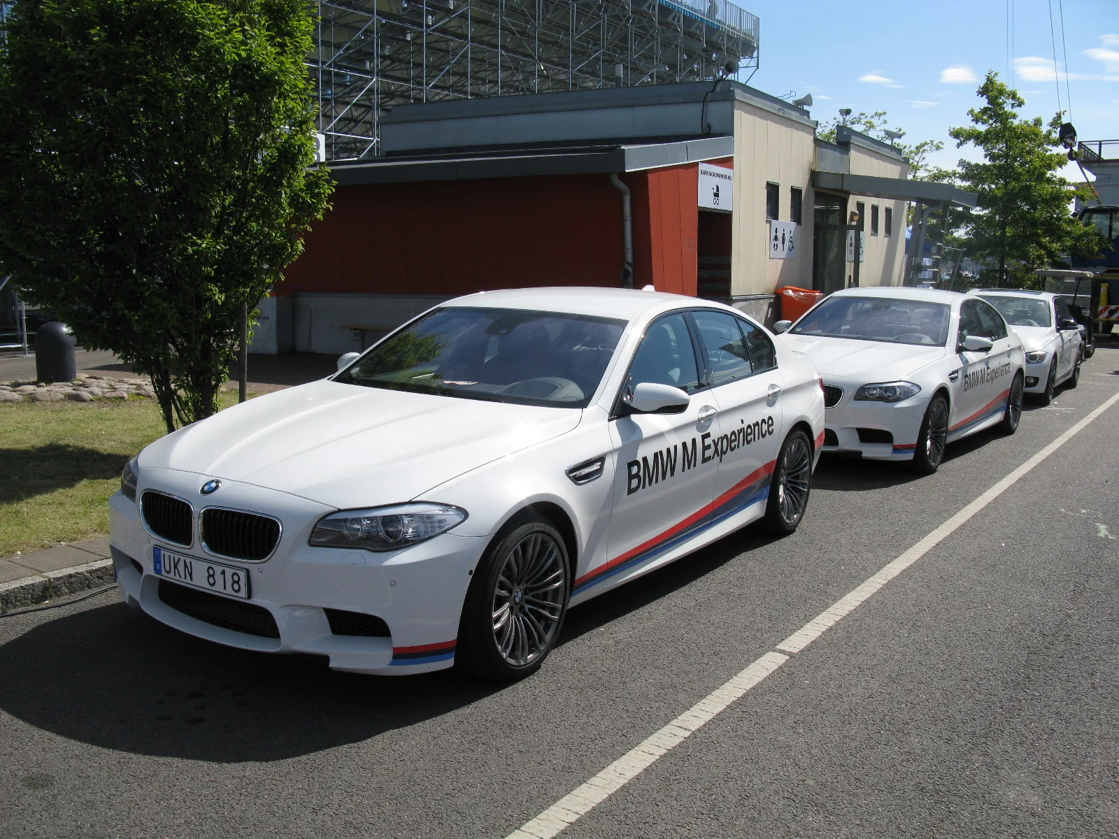 White BMW M5 F10 sedan at an outdoor event, with other BMWs behind it.